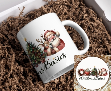 Preview: Weihnachtstasse Christmas Basics Preview: Ein weißer Keramikbecher, verpackt in einer Geschenkbox, liegt auf einer Unterlage aus braunem Papierfüllmaterial. Auf dem Becher ist eine festliche Illustration abgebildet: Ein fröhlich dreinblickender Weihnachtsmann, der ein Rentier liebevoll umarmt. Ne